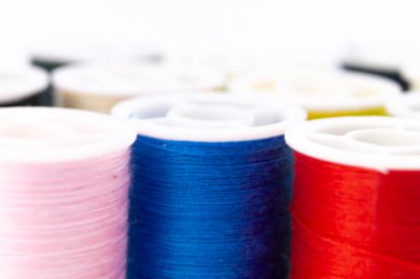 Pembe, mavi, kırmızı ve sarı renkli canlı iplik makaraları yakın plan. Dikiş iplikleri beyaz bir yüzeyde düzgün bir şekilde düzenlenir, renkli bir desen oluşturur.