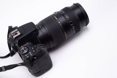 Geniş yakınlaştırma merceğine sahip siyah dijital tek lensli bir kamera, tasarımı ve özelliklerini gösteren temiz beyaz bir zemin üzerine yerleştirilmiştir..