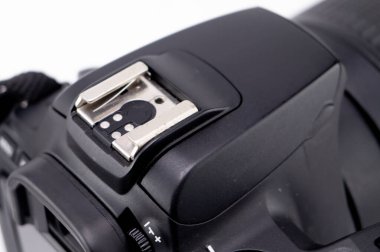 Siyah bir DSLR kameranın yakın plan çekimleri ve gümüş bir ayakkabı montu. Kamera temiz, beyaz bir arkaplana ayarlı..