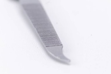 Metal bir tırnak dosyasının detaylı yakın çekimi, desenli yüzeyini gösteriyor ve temiz beyaz bir arkaplana karşı eğri uçlu.