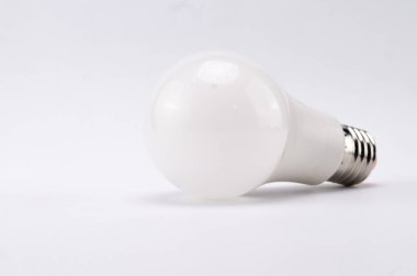 Beyaz bir LED ampulün yakın plan görüntüsü düz beyaz bir zemin üzerinde duruyor, tasarımı ve enerji tasarruflu teknolojisi sergileniyor..