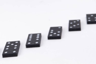 Beyaz noktalı beş siyah domino taşı temiz beyaz arka planda çapraz bir çizgide dizilmiş. Bu da domino etkisi olduğunu gösteriyor..