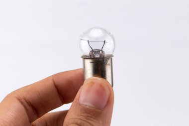 Bir el küçük, temiz bir ampulü tutar. Ampulün görünen bir filamanı ve düz beyaz arkaplan üzerine kurulmuş metalik bir tabanı var..