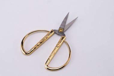 Altın saplı açık makas yakın plan ve beyaz zemin üzerinde keskin bıçaklar, dekoratif tasarım ve hassasiyet kesme aracı göstermektedir.