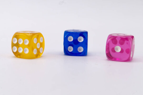 Три кости, желтый, синий и розовый, расположены на белом фоне. Кости показывают различные цифры, представляющие собой игру случая.