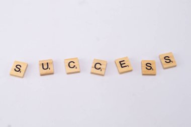 SUCCESS kelimesi, temiz beyaz arkaplandaki ahşap harflerle yazılır, başarıyı ve hedefleri sembolize eder..