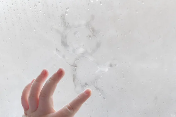 Die Hand des Kindes zeichnet im Winter einen Mann auf ein vernebeltes Fenster — Stockfoto