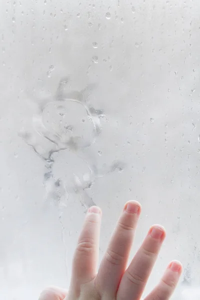 Die Hand des Kindes zeichnet im Winter einen Mann auf ein vernebeltes Fenster — Stockfoto
