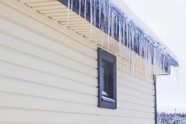 Icicles hang from the roof of a private house in winter — Stock Photo, Image