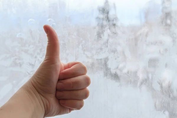 Sign of thumb up hand in front of a frozen window