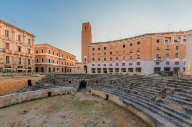 Lecce, Puglia - 11 Ağustos 2025: Barok binalı Roma harabelerinin sahne kompozisyonu, Lecce 'nin bir yaz akşamında katmanlanmış tarih ve kültür mirasını sergilemesi.