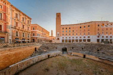Lecce, Puglia - 11 Ağustos 2025: Barok binalı Roma harabelerinin sahne kompozisyonu, Lecce 'nin bir yaz akşamında katmanlanmış tarih ve kültür mirasını sergilemesi.