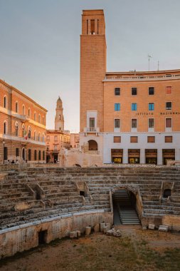 Lecce, Puglia - 11 Ağustos 2025: Arka planda Lecce şehir manzaralı Roma amfitiyatro kalıntıları, kültür mirası ve Akdeniz cazibesini gösteriyor.