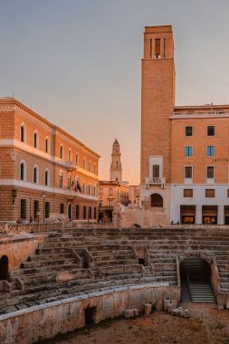 Lecce, Puglia - 11 Ağustos 2025: Barok binalı Roma harabelerinin sahne kompozisyonu, Lecce 'nin bir yaz akşamında katmanlanmış tarih ve kültür mirasını sergilemesi.