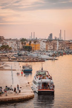 Taranto, İtalya - 16 Ağustos 2025: Şehir silueti ve sanayi bölgesiyle birlikte sıcak akşam ışığı denizi yansıtıyor.