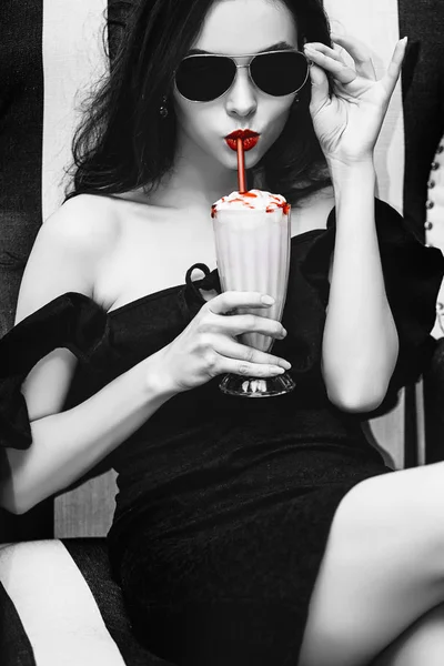 Model young woman beautiful and luxurious sitting with strawberry cocktail in black and white striped chair fashionable and stylish in sunglasses