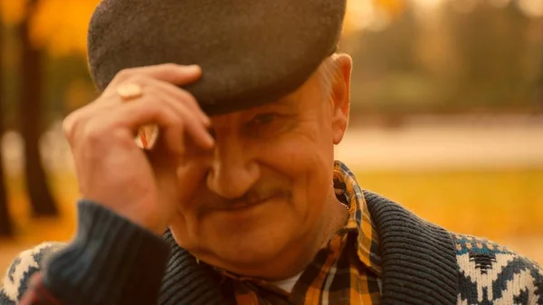 Feliz retrato de homem velho no parque de outono usando boné de lã — Fotografia de Stock