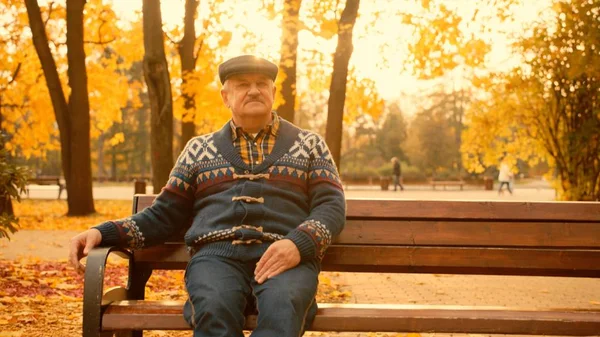 Öreg ember ül a padon, az őszi parkban — Stock Fotó