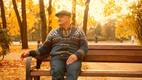 Velho está sentado no banco no parque de outono — Fotografia de Stock