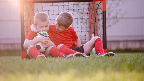 Malý fotbal hráči sedí u fotbalové brány cíl na trávníku — Stock fotografie