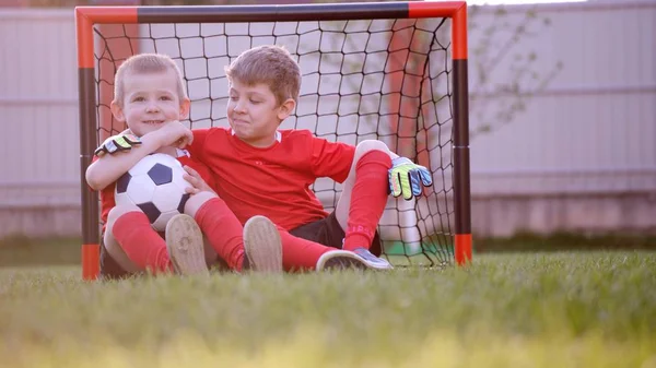 小さなサッカー選手はサッカー ゴールで芝生に座っています。 — ストック写真
