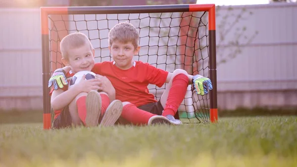 Malý fotbal hráči sedí u fotbal gól na trávníku — Stock fotografie