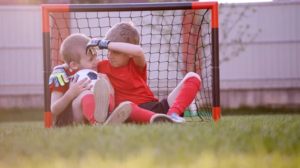 Malý fotbal hráči sedí u fotbal gól na trávníku — Stock fotografie