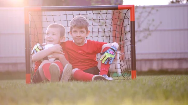 Malý fotbal hráči sedí u fotbal gól na trávníku — Stock fotografie