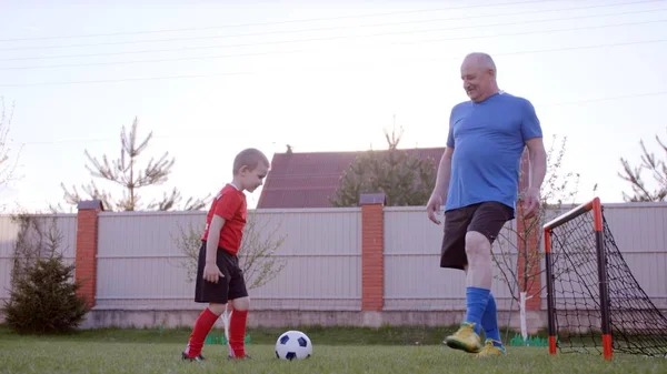 Dědeček se hraje fotbal s jeho vnuk na trávníku v zahradě — Stock fotografie