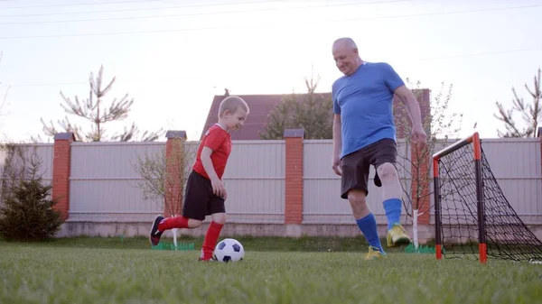 Dědeček se hraje fotbal s jeho vnuk na trávníku v zahradě — Stock fotografie