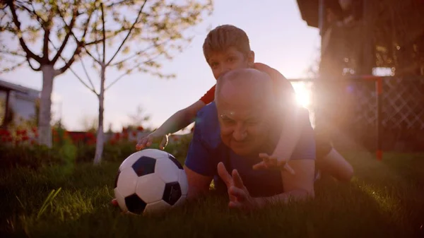 Malý chlapec a jeho dědeček s fotbalovým míčem na trávníku při západu slunce — Stock fotografie