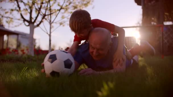 Děda a jeho vnuk hrají fotbalový míč na trávníku — Stock video