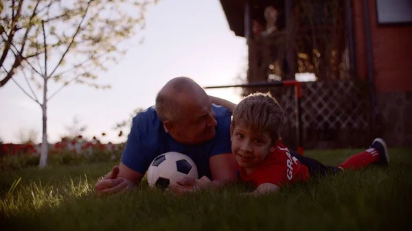 祖父と孫は日没にサッカーボールと芝生の上に横たわっている — ストック写真