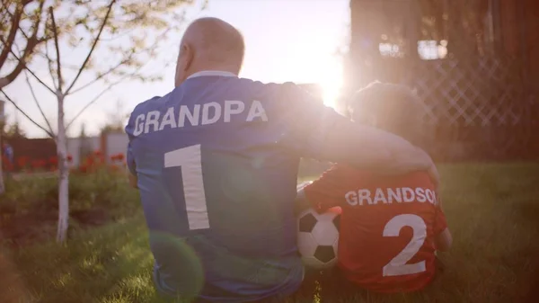 Backshot de abuelo y nieto en el césped con pelota de fútbol en la puesta del sol —  Fotos de Stock
