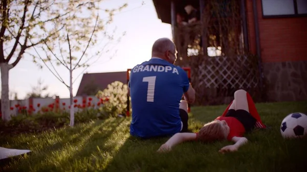 Backshot dědeček a vnuk na trávníku s fotbalovým míčem na západ slunce — Stock fotografie