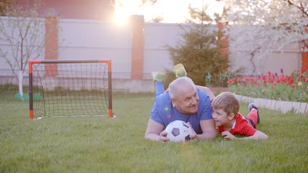 Old man with his grandson are playing football at the backyard