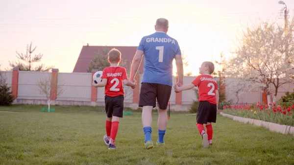 Backshot dědeček je zpracování jeho vnuci, nosí fotbalové dresy, s soccerball — Stock fotografie