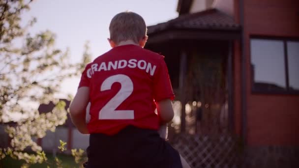 Dos tourné Portrait de grand-père avec son petit-fils sur le cou avec ballon de football — Video