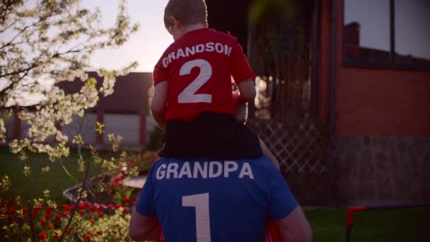 Портрет дедушки с внуком на шее с футбольным мячом — стоковое видео
