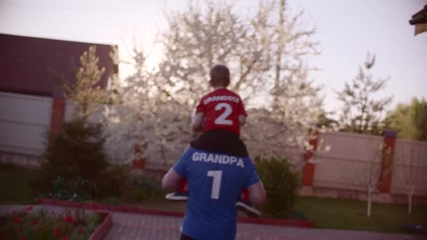 Voltar tiro Retrato do avô com seu neto no pescoço com bola de futebol — Vídeo de Stock