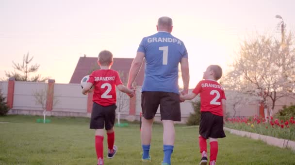 Backshot del abuelo está manejando a sus nietos, con uniforme de fútbol, con balón de fútbol — Vídeo de stock