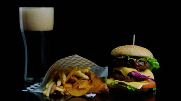 Gießglas mit Coca-Cola und leckerem Burger, Pommes auf schwarzem Hintergrund für Werbezwecke — Stockfoto