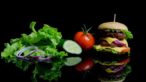 Frisches Gemüse und leckere Burger mit Käse und Rinderschnitzeln auf schwarzem Hintergrund — Stockfoto