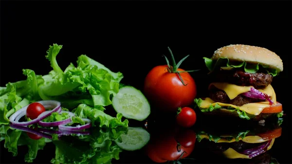 Frisches Gemüse und leckere Burger mit Käse und Rinderschnitzeln auf schwarzem Hintergrund — Stockfoto