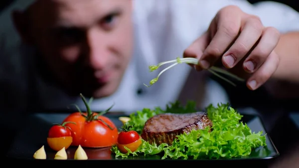 Chef está terminando el delicioso plato de carne con verduras. Chef está fuera de foco en el fondo —  Fotos de Stock