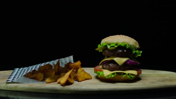 Κοντινό πλάνο της νόστιμο burger με διπλό τυρί και τηγανιτές πατάτες. Μαύρο φόντο — Αρχείο Βίντεο