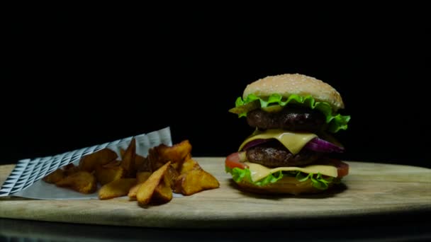 Nahaufnahme von leckeren Burgern mit Doppelkäse und Pommes frites. schwarzer Hintergrund — Stockvideo