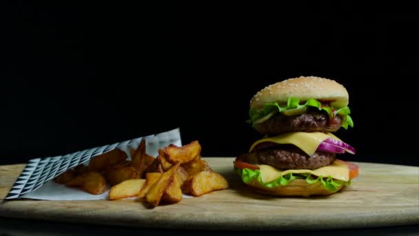 Primer plano de deliciosa hamburguesa con doble queso y papas fritas. Fondo negro — Vídeos de Stock