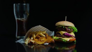 Coca-cola ve lezzetli hamburger, patates kızartması ticari için siyah arka plan üzerine dökerek cam