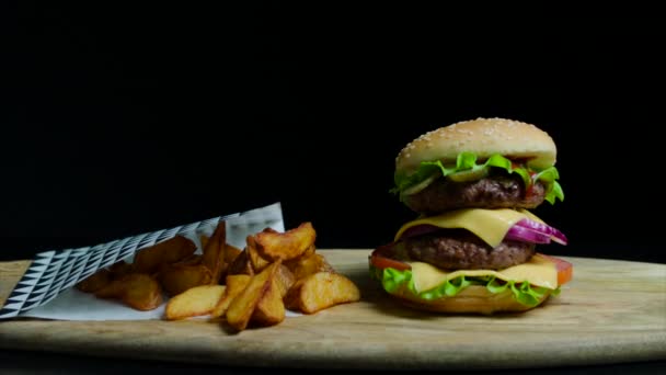 Primer plano de deliciosa hamburguesa con doble queso y papas fritas. Fondo negro — Vídeos de Stock